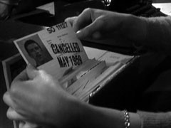 Miss Brisket pulls out Mark’s identity card, numbered SO 11127; it is stamped CANCELLED MAY 1959