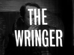 title card: white all caps text reading ‘THE WRINGER’ superimposed on Hal anxiously holding his hand to his mouth as he sits in the train
