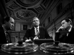 Charles sits between Hal and Steed, all three in suit and tie, as Hal outlines the allegations against Steed. A reel to reel tape, out of focus in the extreme foreground, records the conversation