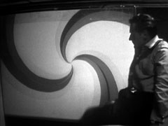 Steed stares at one of the brainwashing images, a hypnotising spiral, projected onto the wall outside his wire cage