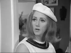 Georgie, dressed as Mrs. Peel, turns to speak to Steed