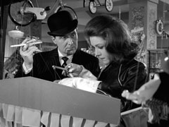 Steed and Emma exchange information as she pretends to demonstrate a marionette theatre