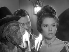 Steed and Mrs. Peel, in period dress, survey the orgy; Steed gets a better look by peering through his eyeglass