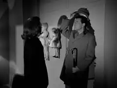 Steed stands in the hole made by the cybernaut, raising his hat above his head to indicate how much taller the cybernaut is
