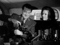 Steed and Emma, seated in the back of a cab, sample one of the bottles they liberated from Boardman’s cellar