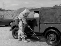 A soldier wearing a hazardous material suit sprays the wheels and undercarriage of a Landrover to prevent the spread of contamination