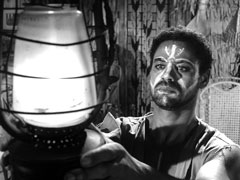Razafi, his face painted with a tribal marking, lights a hurricane lantern in the foreground left