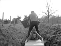 Steed dives under Baron’s legs as they fight on top of the miniature train