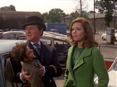 Steed and Mrs Peel visit the yard where Dusty’s car is being examined - Steed hold Dusty’s ventriloquist’s dummy while Emma stands to his left in a fetching green ensemble