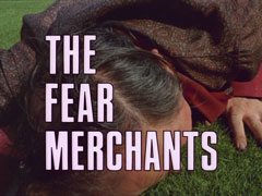 title card: white all caps text with black dropshadow to the left reading ‘THE FEAR MERCHANTS’ superimposed on a close-up of Meadows lying face-down on the turf in fear