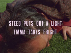 subtitle card: white all caps text with black dropshadow to the left reading ‘STEED PUTS OUT A LIGHT
			EMMA TAKES FRIGHT’ superimposed on a close-up of Meadows lying face-down on the turf in fear