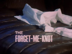title card: white all caps text reading ‘THE FORGET-ME-KNOT’ superimposed on a knotted handkerchief lying forgotten on the seat of a taxi