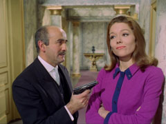 Mrs. Peel refuses to co-operate despite Brodny trying to coerce her with a pistol as they stand in the marble hallway of the embassy