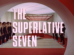 title card: white all caps text with black dropshadow to the left reading ‘THE SUPERLATIVE SEVEN’ superimposed on a view through a red and white circular door of ranks of male and female martial artists dressed in black, flanking a dead man lying on a mat between them; a red lattice hangs from the ceiling in the background, before white curtains