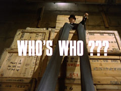 title card: white all caps text reading ‘WHO’S WHO???’ superimposed on a low angle view of the enormously long stilt legs of the dead Hooper, perched up on a stack of crates in a warehouse