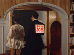Steed and Tara leave his apartment to go to dinner, she in a very short silk dress, he in a rented tuxedo that has a light-up sign on his back which reads Eat at JOE’S in red cursive on a white square