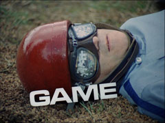 title card: white all caps text reading ‘GAME’ on a slight angle, superimposed on a close-up of the dead racing driver’s head, his goggles filled with jigaw pieces