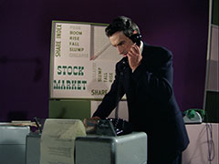 Dexter stands in front of the stock market game, getting stock prices from a telephone