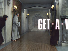 title card: white all caps text reading ‘GET - A W’ superimposed on three cowled monks staring down the empty grey stone corridor; the text is scrolling off to the right