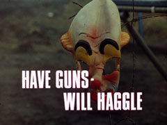 title card: white all caps text reading ‘HAVE GUNS - WILL HAGGLE’ superimposed on a rubber clown mask hanging from a broken barbed wire fence