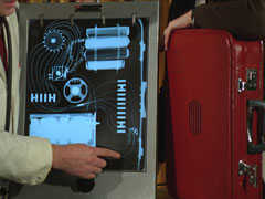 The suitcase stands on its side beside a lightbox showing an x-ray of its contents