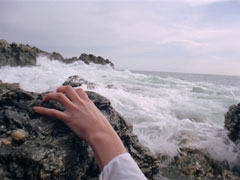 Tara’s hand appears, clawing at a rock as she tries to pull herself from the raging surf at the base of the cliff