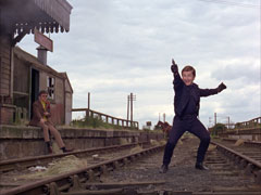 Grant practices his sharp-shooting at the abandoned railway station and Farrington looks on in a bored fashion