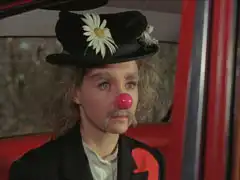 Miranda sits in the back of Steed’s car in her clown disguise; he’s just suggested she remove it.