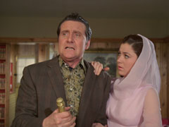 Tara, wearing a pale pink dress and headscarf, puts her hand on Steed’s shoulder