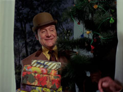 Steed stands at the front door with a pile of presents and a small Christmas tree