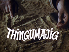 title card: white text reading ‘Thingumajig’ in a script font superimposed on the box shape drawn in the sand by Greer, whole hands lie beside it